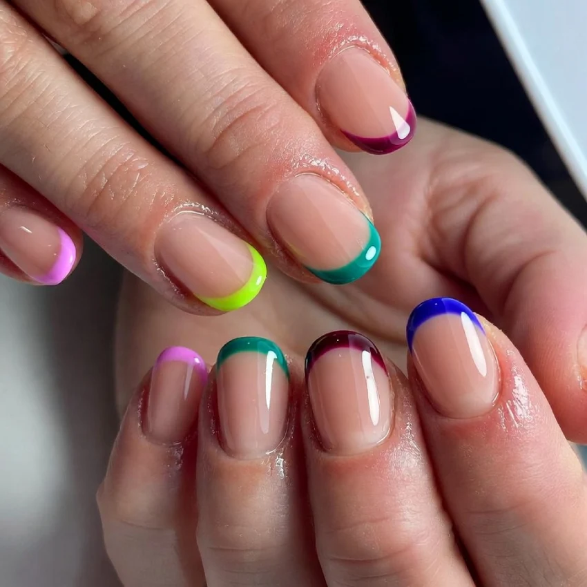 Close-up of colored French tip nails, each with a different vibrant shade including pink, yellow, green, blue, and purple on a nude base.