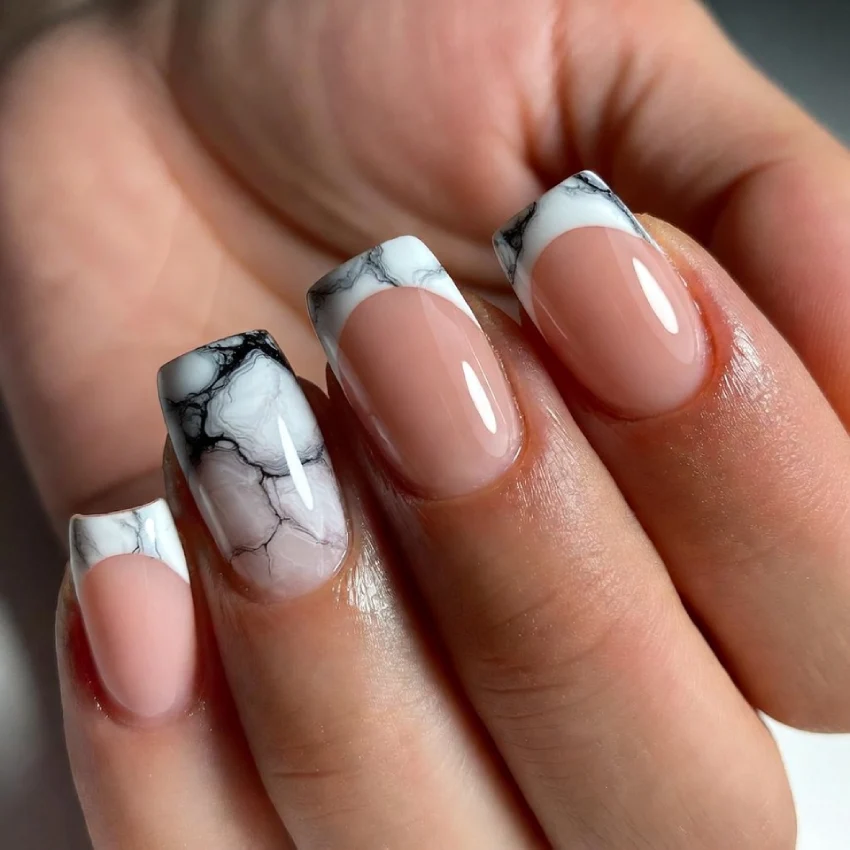 Close-up of marble French tip nails with white and black stone patterns on the tips and a nude glossy base.