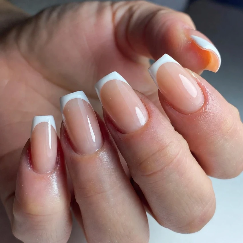 Close-up of ombre French tip nails with a nude-to-white gradient on square-shaped nails, glossy finish, elegant manicure.