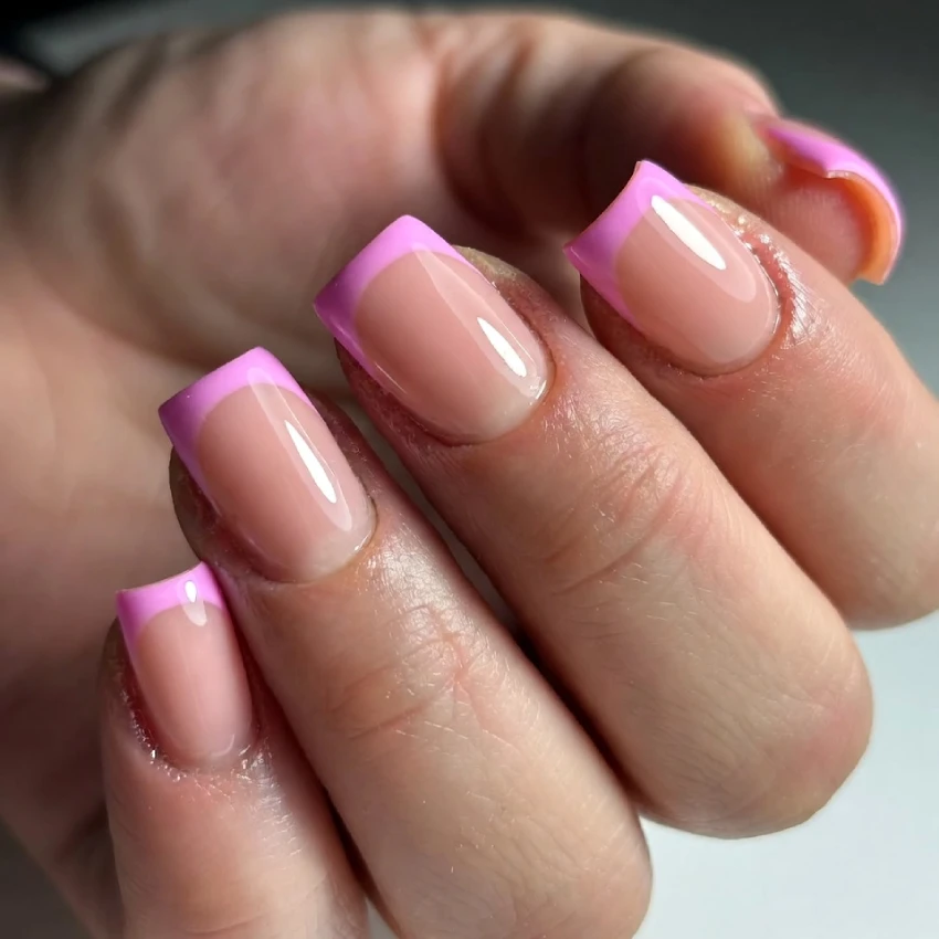 Close-up of pink French tip nails with a nude base, glossy finish, and square shape, showing a stylish and feminine manicure.