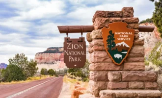 Zion National Park entrance sign with red rock cliffs and scenic road in southern Utah.