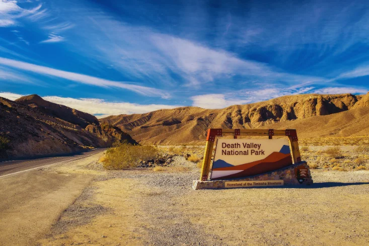 Entrance sign to Death Valley National Park with desert mountains and clear blue sky in the background.