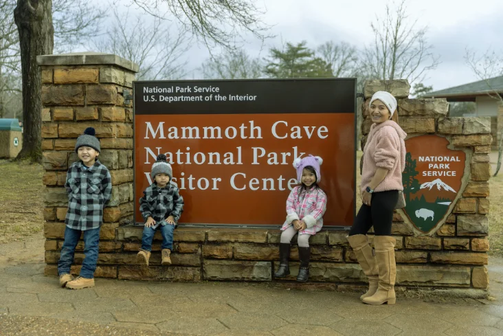 Family posing in front of the Mammoth Cave National Park Visitor Center sign with children in winter clothing.