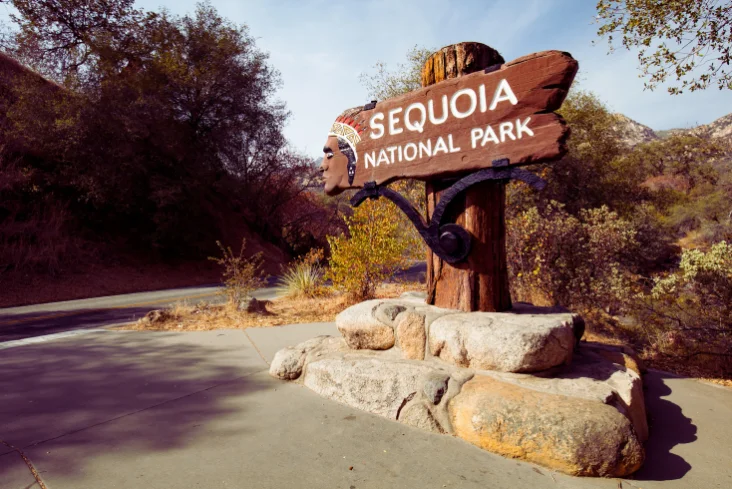 Sequoia National Park wooden entrance sign with carved Native American figure and forest in the background.
