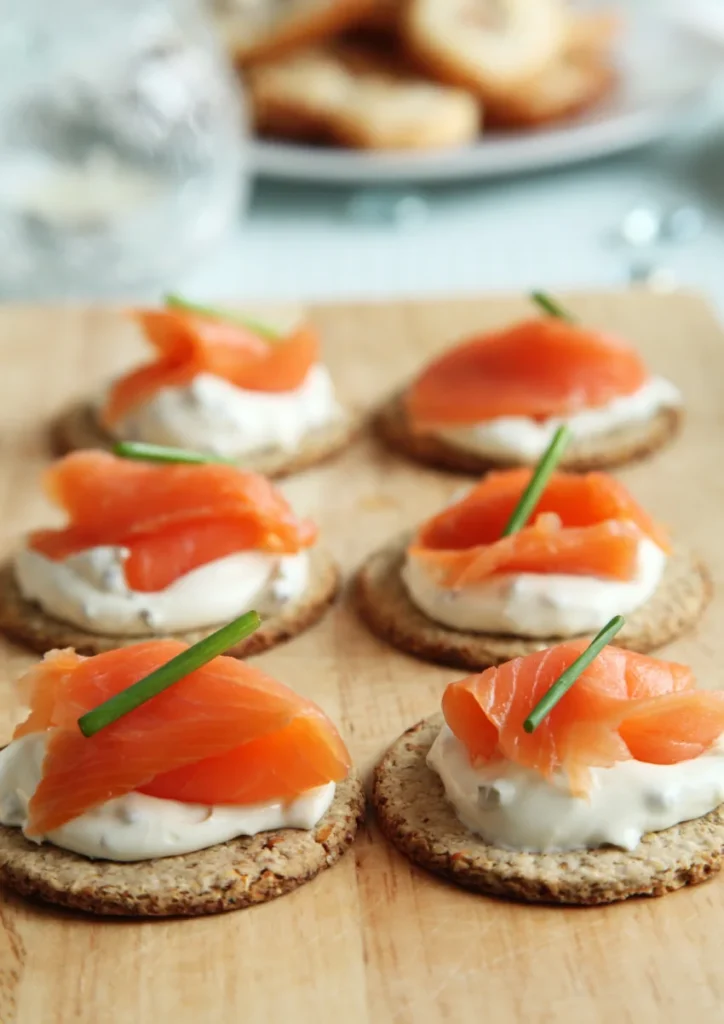 Smoked salmon appetizers on round crackers topped with cream cheese and fresh dill, arranged neatly on a white plate.