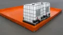 High-resolution image of two IBC containers placed on an orange spill containment berm in an industrial setting